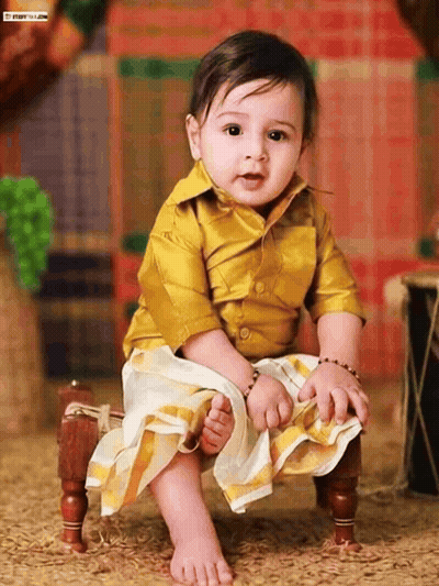 A Baby Wearing A Yellow Shirt And White Skirt Is Sitting On A Small Wooden Chair GIF