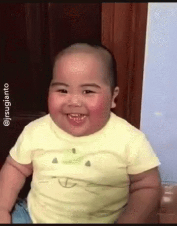 A Baby Wearing A Yellow Shirt With An Apple On It Smiles GIF