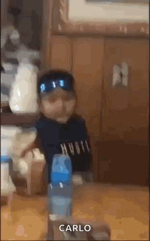 A Baby Wearing Sunglasses Is Sitting At A Table With A Bottle Of Water And Says Carlo . GIF
