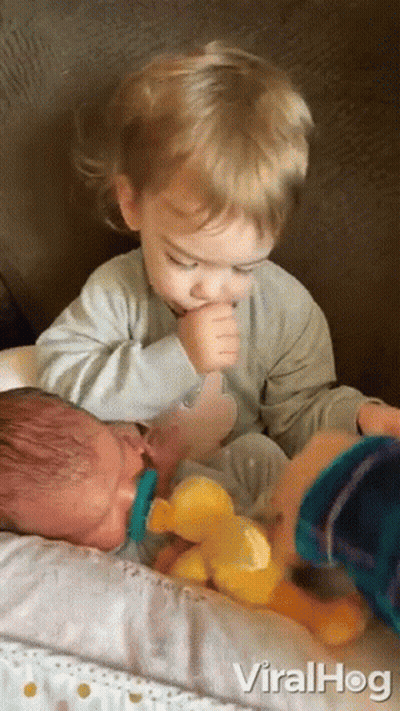 A Baby With A Pacifier In His Mouth Is Being Held By A Young Boy . GIF