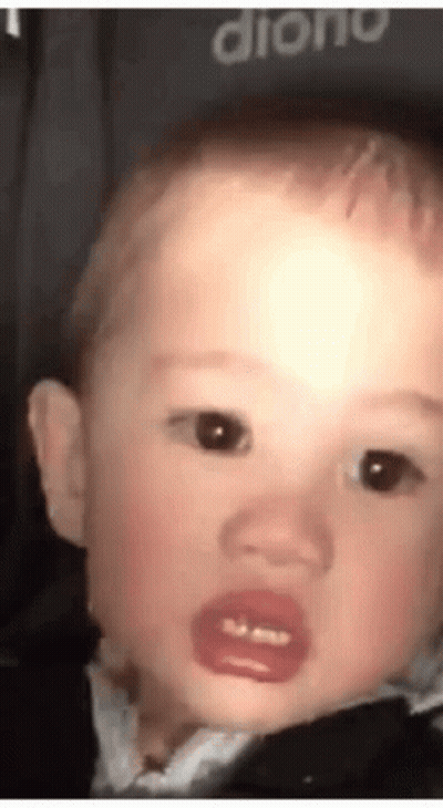 A Baby With A Pacifier In His Mouth Is Making A Funny Face And Looking At The Camera . GIF