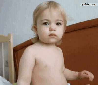 A Baby Without A Shirt Is Standing In Front Of A Bed With The Website Gfbir.com Visible In The Corner GIF