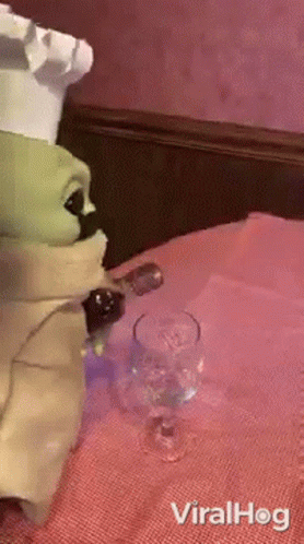 A Baby Yoda Figurine Is Sitting At A Table With A Glass Of Wine And A Bottle Of Wine . GIF