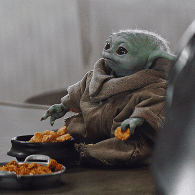 A Baby Yoda Is Sitting At A Table With A Bowl Of Chicken Nuggets GIF