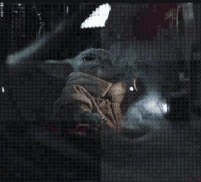 A Baby Yoda Is Sitting In A Dark Room With A Light Shining On It GIF
