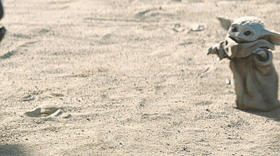 A Baby Yoda Toy Is Standing In The Sand Looking At Something GIF