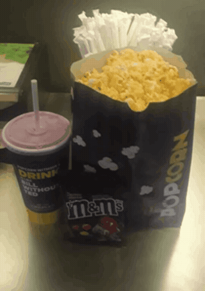 A Bag Of M & M 'S Sits Next To A Bag Of Popcorn On A Table GIF