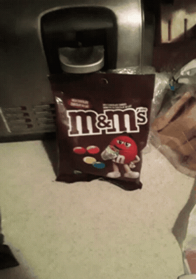 A Bag Of M & M 'S Sits On A Counter In Front Of A Coffee Maker GIF