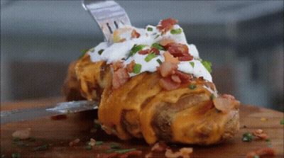 A Baked Potato Covered In Cheese Bacon Sour Cream And Green Onions GIF