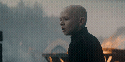 A Bald Boy Stands In Front Of A Fire With His Mouth Open GIF