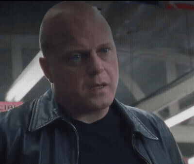 A Bald Man In A Black Jacket Looks Up At Something GIF