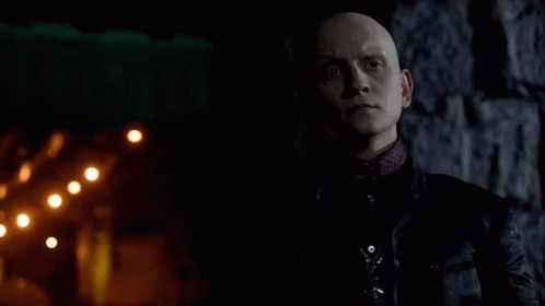 A Bald Man In A Black Jacket Stands In Front Of A Brick Wall GIF