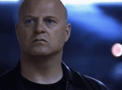 A Bald Man In A Black Shirt And Black Jacket Looks At The Camera GIF