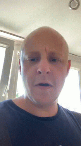 A Bald Man In A Black Shirt Is Looking At The Camera GIF