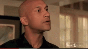 A Bald Man In A Black Shirt Is Standing In Front Of A Window In A Living Room . GIF