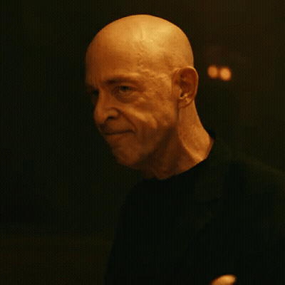 A Bald Man In A Black Shirt Is Waving His Hand In The Dark GIF