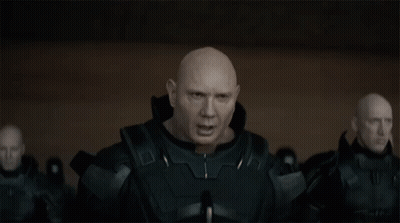 A Bald Man In A Black Suit Is Standing In Front Of A Group Of Bald Men GIF