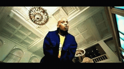 A Bald Man In A Blue Jacket Is Standing In A Room With A Chandelier . GIF