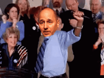 A Bald Man In A Blue Shirt And Tie Holds A Microphone In Front Of A Crowd GIF