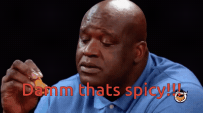 A Bald Man In A Blue Shirt Is Holding A Piece Of Food And Says " Damn Thats Spicy " In Red GIF