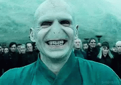 A Bald Man In A Blue Shirt Is Smiling In Front Of A Crowd Of People . GIF