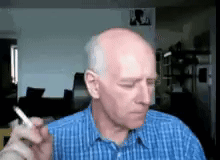 A Bald Man In A Blue Shirt Is Smoking A Cigarette . GIF