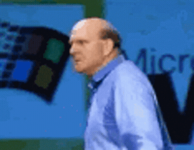 A Bald Man In A Blue Shirt Is Standing In Front Of A Microsoft Sign . GIF