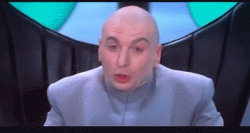 A Bald Man In A Blue Suit Is Making A Funny Face And Looking At The Camera . GIF