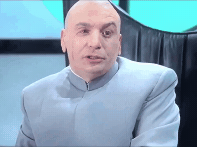 A Bald Man In A Blue Suit Is Sitting In A Chair And Looking At The Camera . GIF
