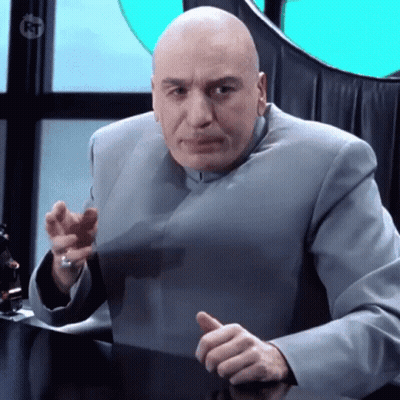 A Bald Man In A Gray Suit Is Sitting At A Desk And Giving A Thumbs Up Sign GIF