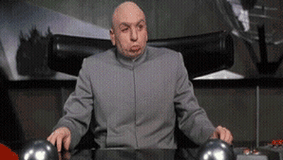A Bald Man In A Gray Suit Is Sitting At A Desk Making A Funny Face GIF