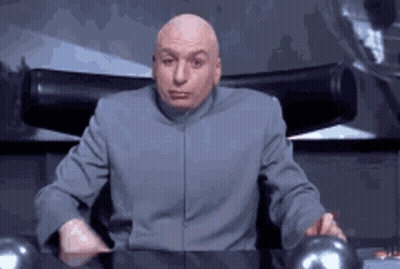 A Bald Man In A Gray Suit Is Sitting In A Chair And Making A Face . GIF