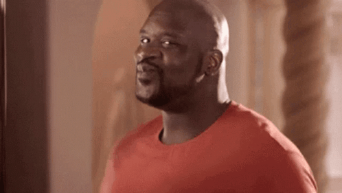 A Bald Man In A Red Shirt Is Standing In Front Of A Punching Bag And Smiling . GIF