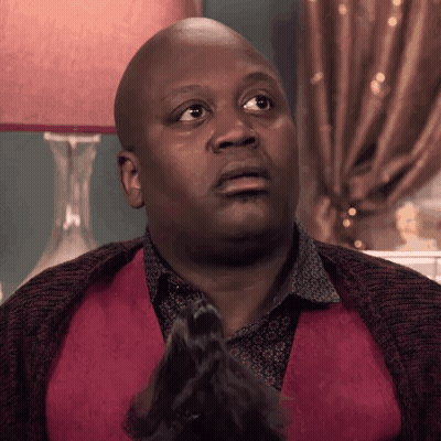 A Bald Man In A Red Vest Is Sitting In Front Of A Lamp And Making A Funny Face . GIF