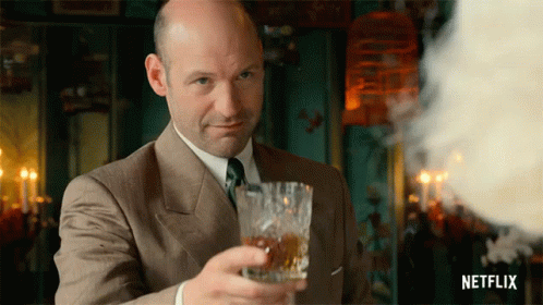 A Bald Man In A Suit And Tie Holds A Glass Of Whiskey GIF