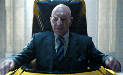 A Bald Man In A Suit And Tie Is Sitting In A Chair GIF