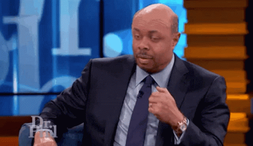 A Bald Man In A Suit And Tie Is Sitting In Front Of A Microphone . GIF