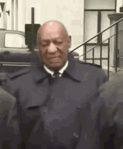 A Bald Man In A Suit And Tie Is Standing Next To A Group Of People . GIF