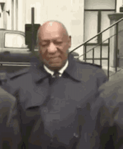 A Bald Man In A Suit And Tie Is Standing Next To A Group Of People . GIF