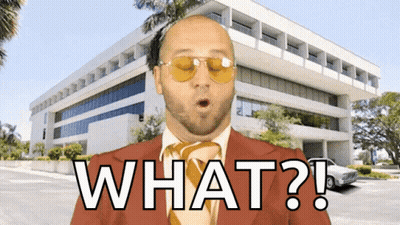 A Bald Man In A Suit And Tie Says What In Front Of A Large Building GIF
