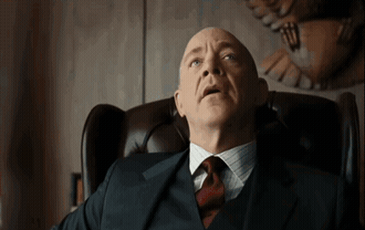 A Bald Man In A Suit And Tie Sits In A Chair GIF