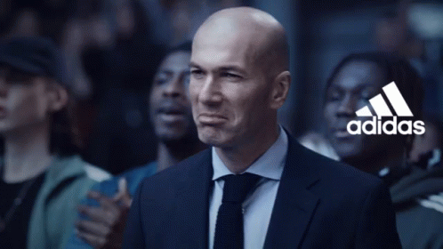 A Bald Man In A Suit And Tie Stands In Front Of A Crowd With The Adidas Logo In The Background GIF