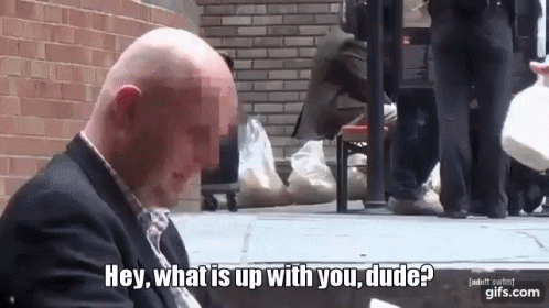 A Bald Man In A Suit Is Sitting On The Sidewalk And Says Hey What Is Up With You Dude GIF