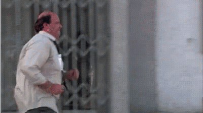 A Bald Man In A White Shirt And Tie Is Running Across A Street . GIF