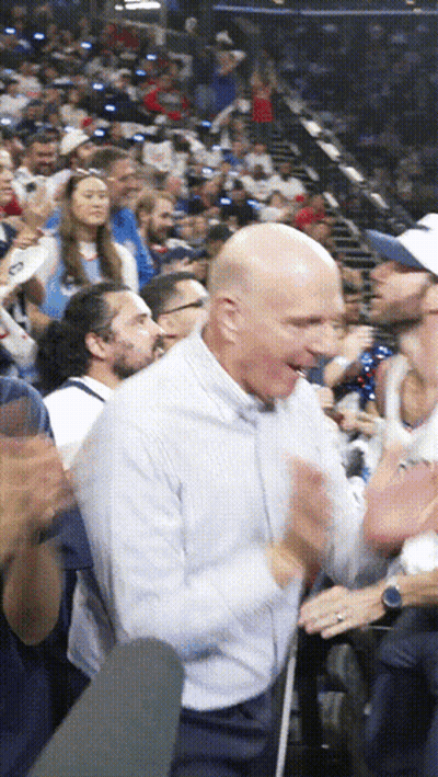 A Bald Man In A White Shirt Is Clapping His Hands In A Crowd GIF