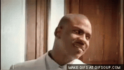 A Bald Man In A White Shirt Is Smiling In Front Of A Door . GIF
