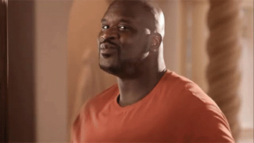 A Bald Man In An Orange Shirt Is Looking At The Camera And Smiling . GIF