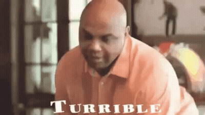 A Bald Man In An Orange Shirt Is Sitting On A Couch And Looking At The Camera . GIF