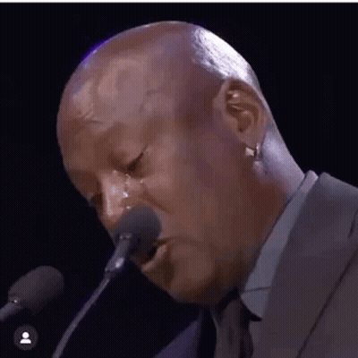 A Bald Man Is Crying While Talking Into A Microphone . GIF