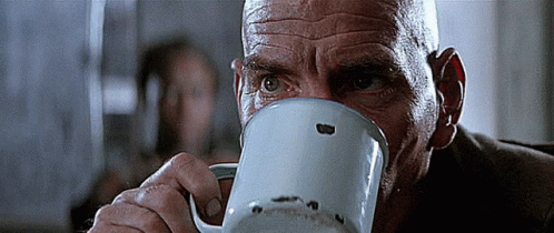 A Bald Man Is Drinking From A White Mug With A Hole In The Middle Of It GIF